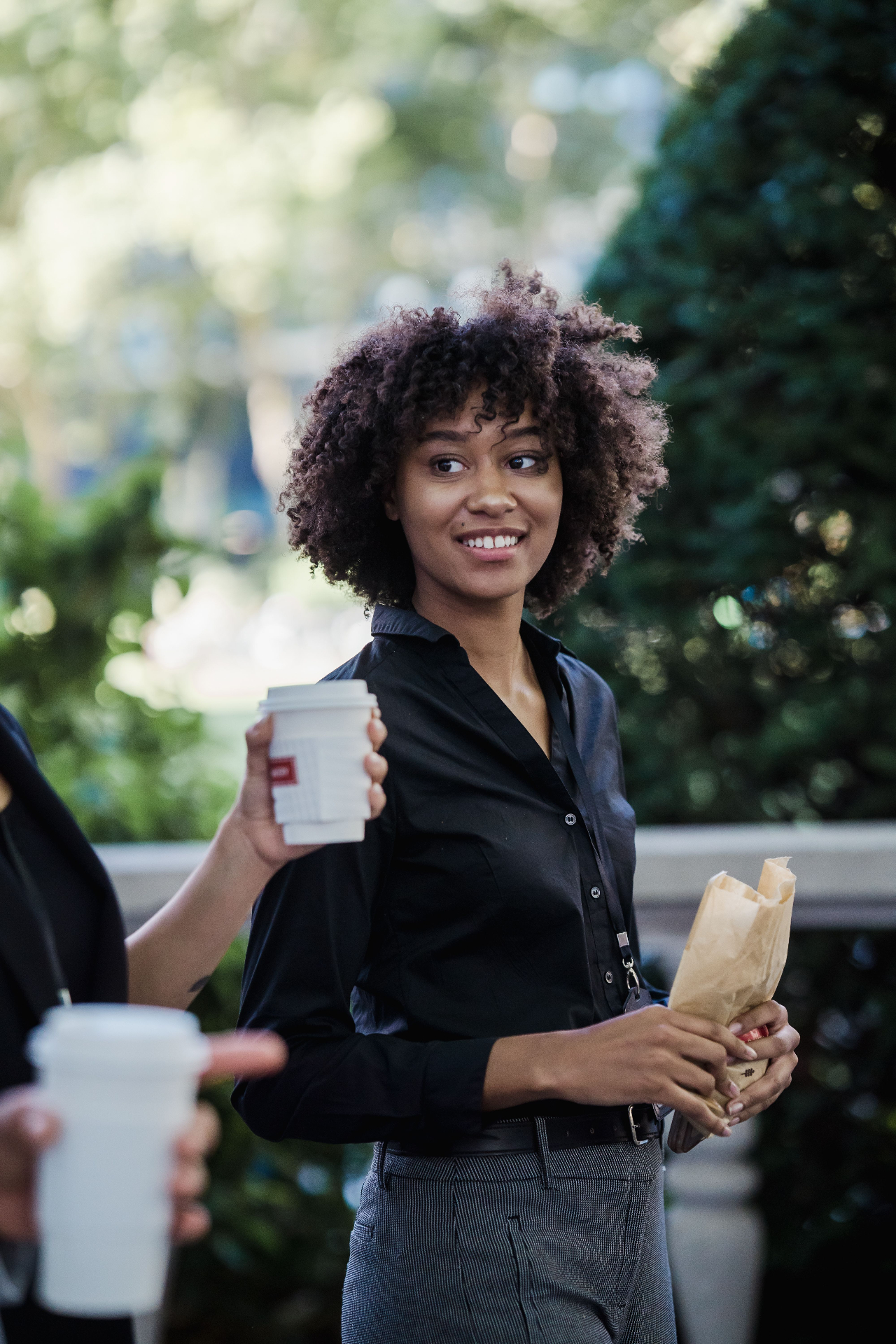 A smiling professional woman holding a coffee cup and snack outdoors, representing everyday wellness.